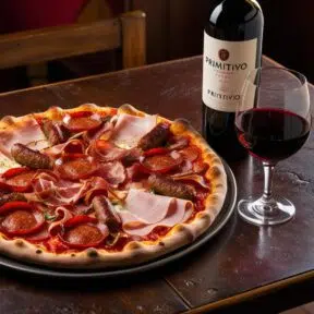 Meat lovers pizza with Italian Primitivo red wine served on a rustic wooden table